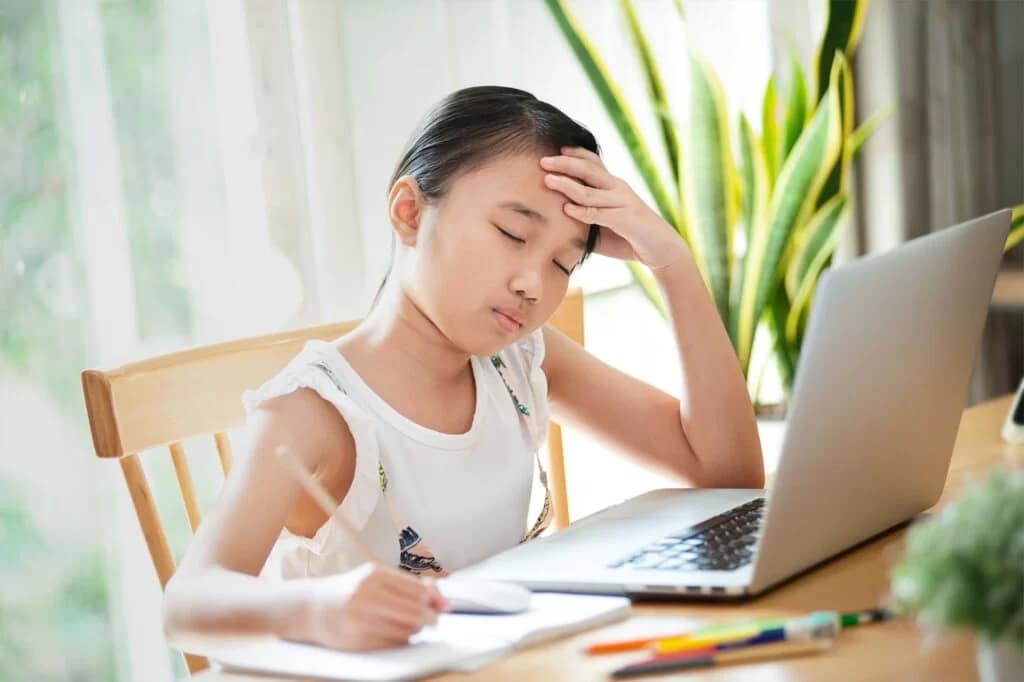 Young girl with hand on forehead looking stressed while studying at a laptop