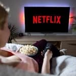 Person watches Netflix with popcorn, holding remote.