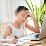 Young girl with hand on forehead looking stressed while studying at a laptop
