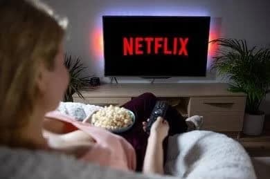 Person watches Netflix with popcorn, holding remote.